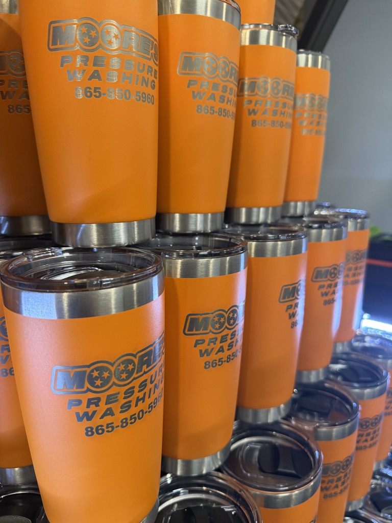 Stack of orange tumblers engraved with Moore's Pressure Washing branding — bulk production run