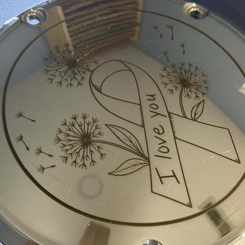 Chrome motorcycle derby cover engraved with an awareness ribbon, dandelions and a personal message