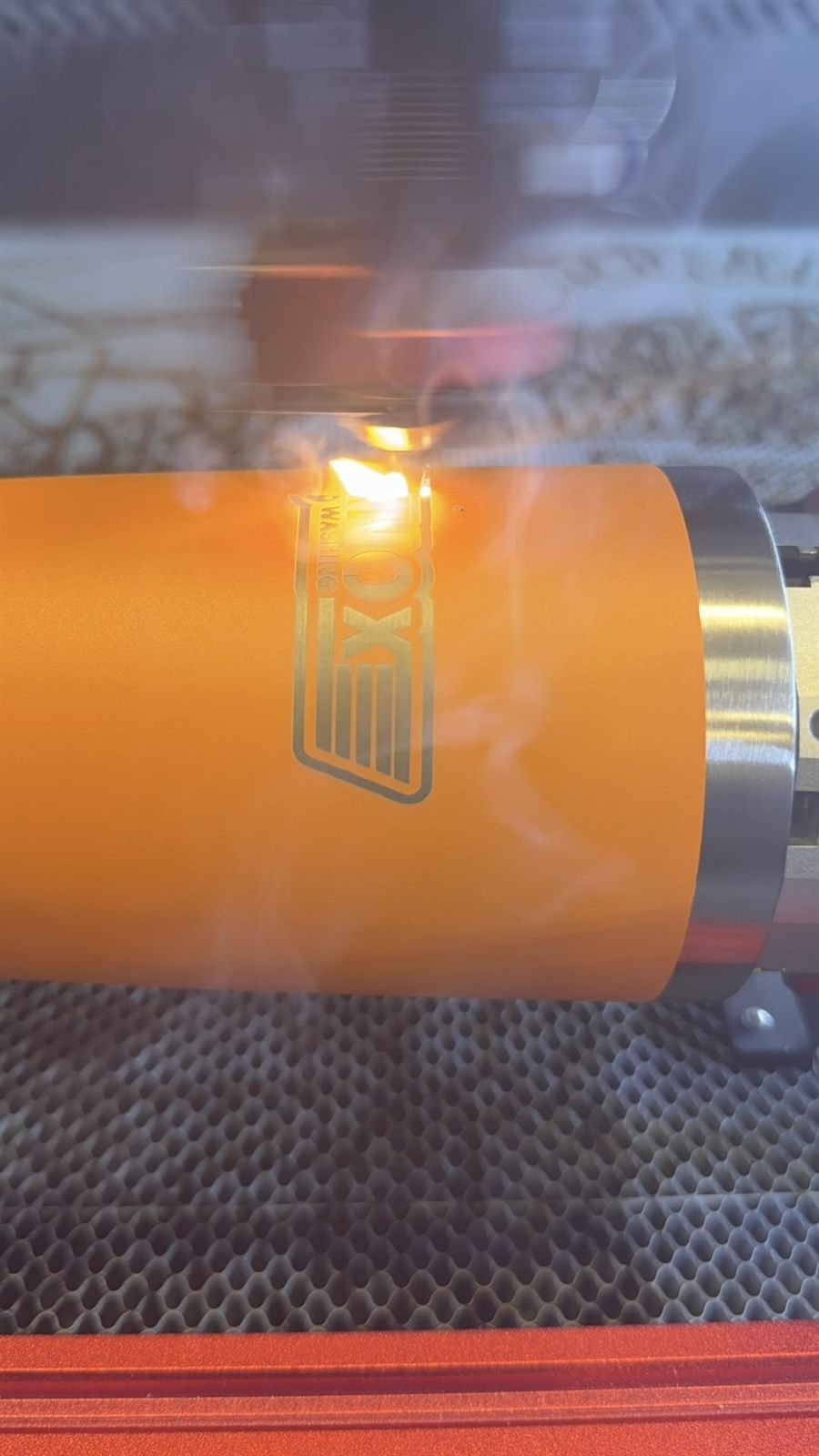 Laser burning custom logo onto orange tumbler